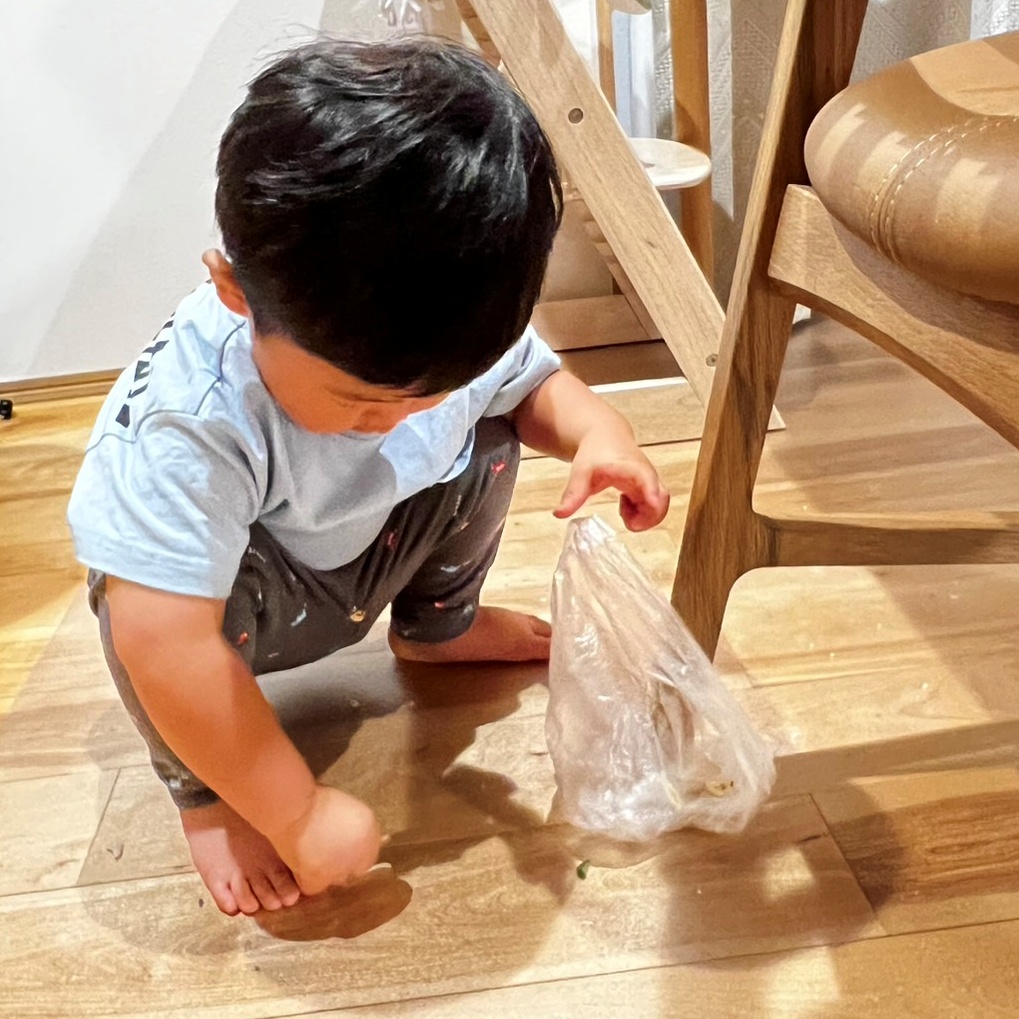 1歳児が食べこぼしをビニール袋で集め手伝いをしている